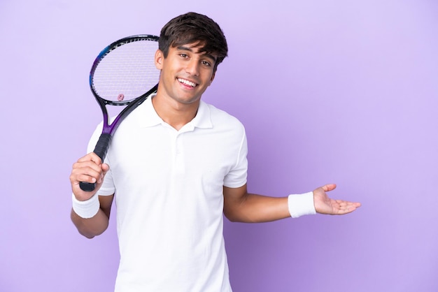 Handsome young tennis player man isolated on ocher background extending hands to the side for inviting to come