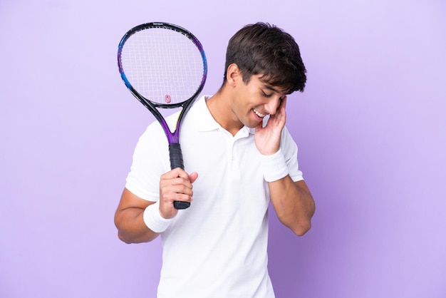 Handsome young tennis player man isolated on ocher background laughing