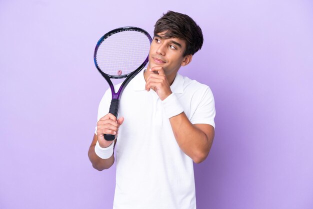 Handsome young tennis player man isolated on ocher background and looking up