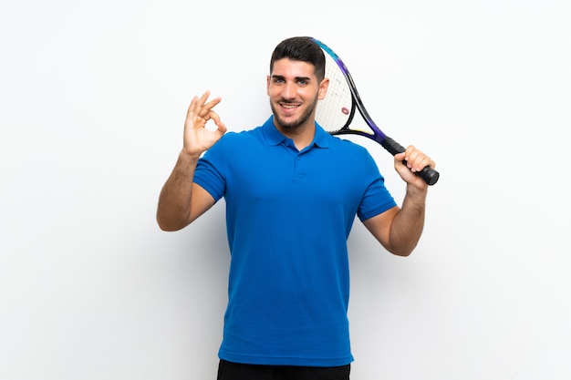 Handsome young tennis player man over isolated white wall showing ok sign with fingers