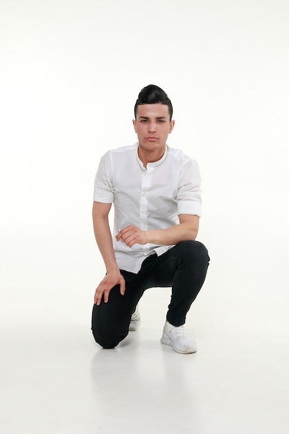 Handsome, young, trendy man is sitting on the floor in studio on gray background. Sitting handsome man