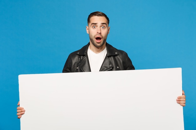 Handsome young unshaven man hold big white empty blank billboard for promotional content isolated on blue wall background studio portrait. People sincere emotions lifestyle concept. Mock up copy space