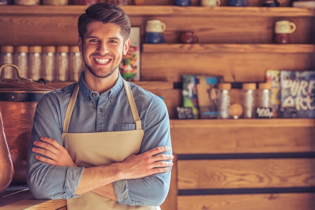 Handsome young waiter in apron is looking at camera.