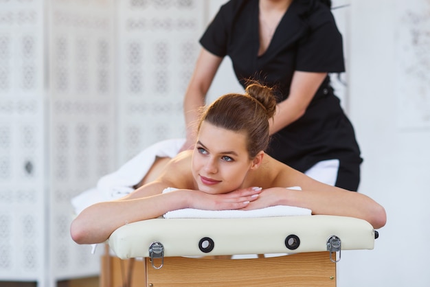 Handsome young woman during massage on the back in spa salon.