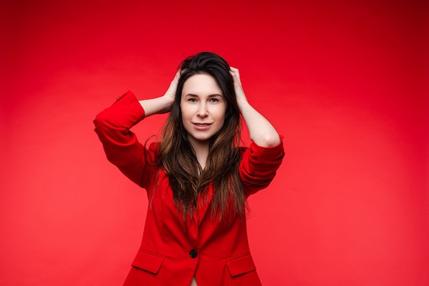 Handsome young woman touches her hair, picture isolated on red wall