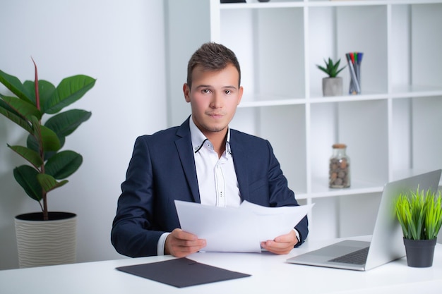 Handsome young worker working in a company office with documents and a laptop