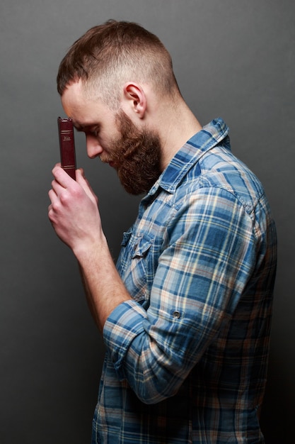 Handsone man reading and praying over Bible in a dark room over gray texture