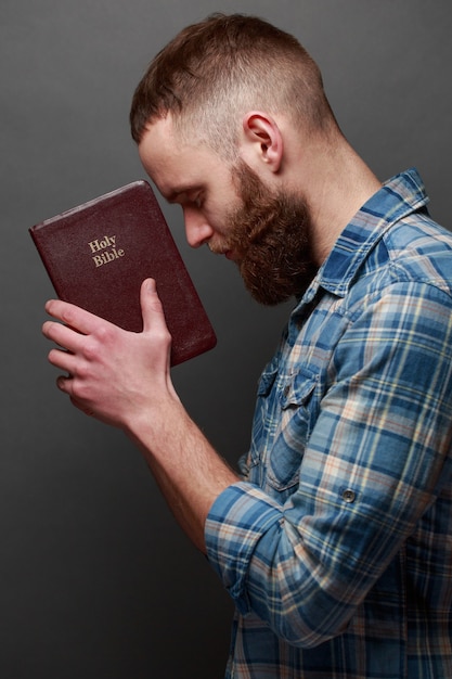 Handsone man reading and praying over Bible in a dark room over gray texture