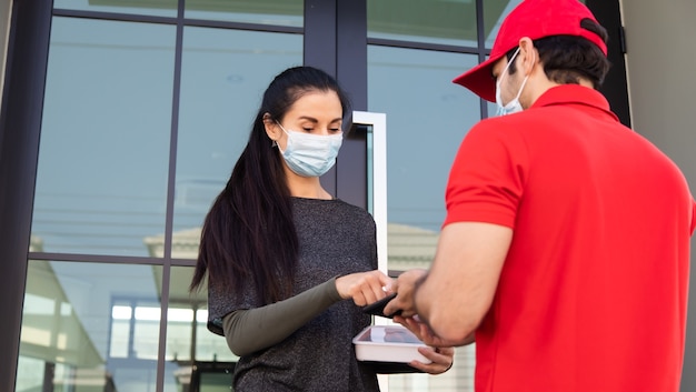 Handtekening op smartphone-apparaat ondertekenen om een pakket te krijgen. vrouw die pakket ontvangt van bezorger in rood uniform