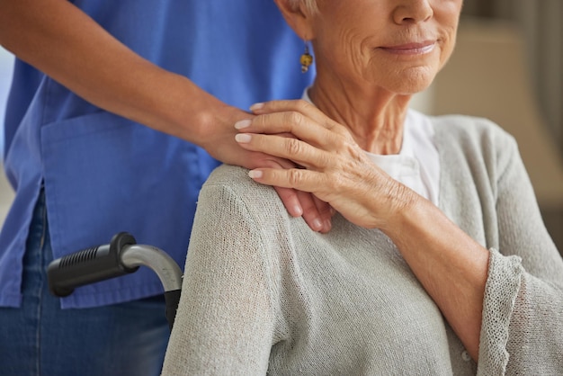 Handverpleegkundige en bejaarde patiënt met een handicap hand in hand thuiszorgmedewerker voor empathie vriendelijkheid en ondersteuning in de gezondheidszorg Verzorger vrijwilliger en vertrouwen hulp voor oudere vrouw in rolstoel