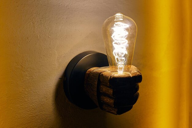 Handvormige kroonluchter met gloeiende gloeilamp op gele muur