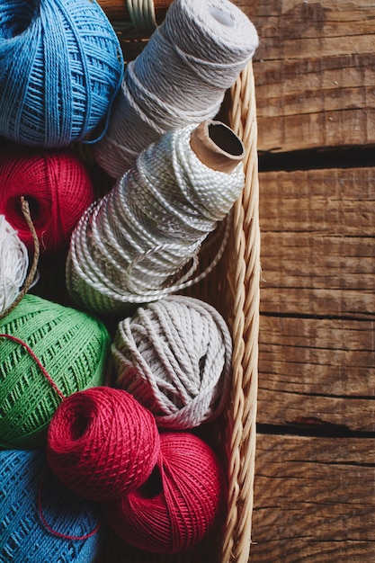 Handwerken, macramé, breien. Garens en draden van felle kleuren in een rieten mand op een houten ondergrond. Vrouwenhobby.