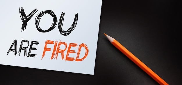 Handwriting announcement text showing you are fired business\
concept for unemployed or discharge written on notepad paper\
background with space office view with pencil marker