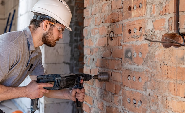 Handyman at a construction site in the process of drilling a wall with an perforator.