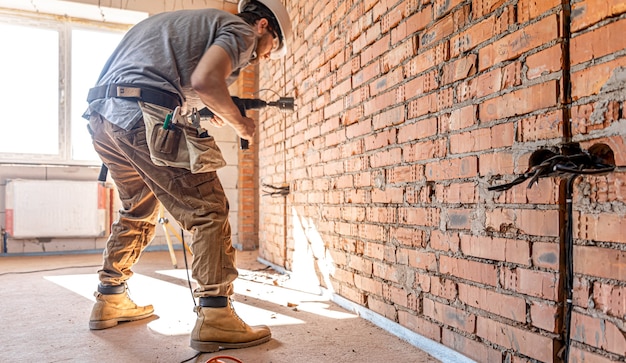 Handyman at a construction site in the process of drilling a wall with a perforator