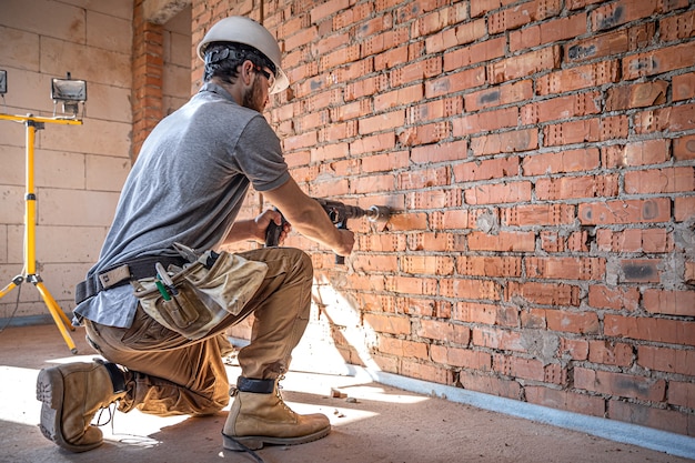 Handyman at a construction site in the process of drilling a wall with a perforator