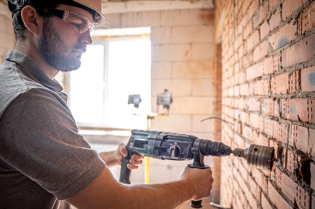 Handyman at a construction site in the process of drilling a wall with a perforator.