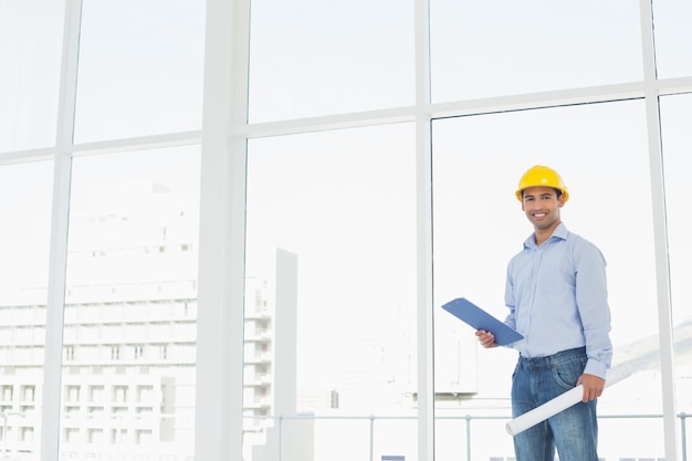 Handyman in hard hat with clipboard and blueprint in office