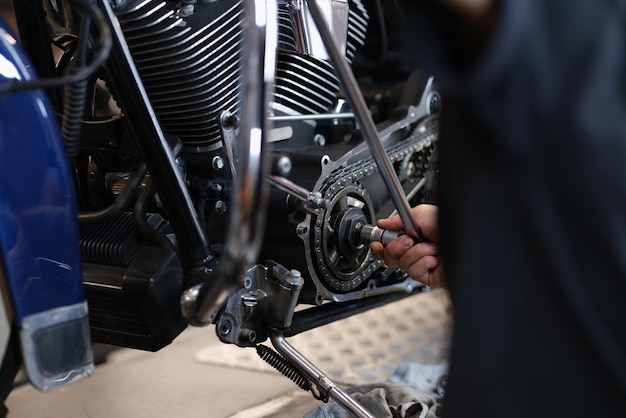 Механик-разнорабочий ремонтирует часть мотоциклетного транспорта с помощью гаечного ключа