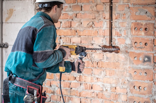 Handyman in the process of drilling a wall with a perforator.