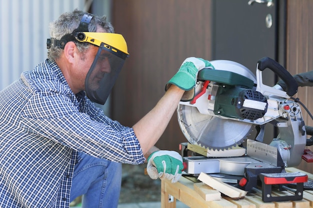 A handyman in a protective helmet works with a miter saw