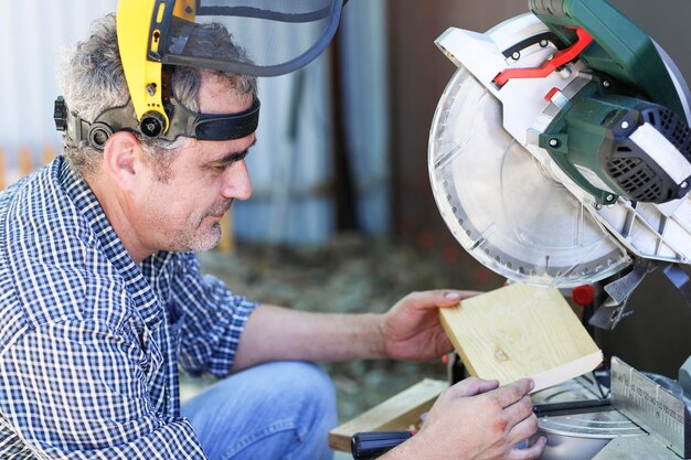 A handyman in a protective helmet works with a miter saw