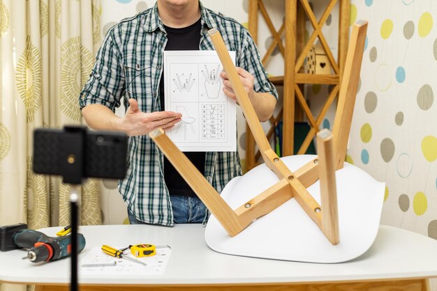 Photo handyman shows assembling chair shooting video instructions on smartphone