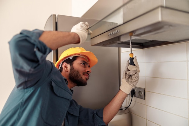 Handyman in uniform repairing kitchen extractor replacing filter in cooker hoodMaintenance concept