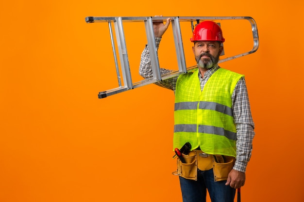 Foto tuttofare in uniforme in piedi con scala su sfondo arancione