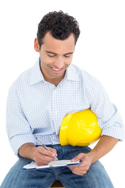 Handyman with yellow hard hat writing in clipboard