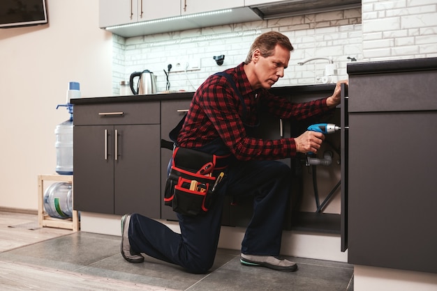 Photo handyman at work repairing kitchen shelves by perforator