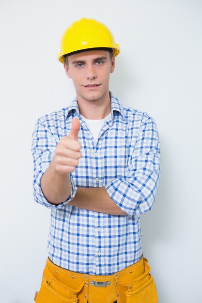 Foto tuttofare nel cappello giallo che gesturing i pollici in su