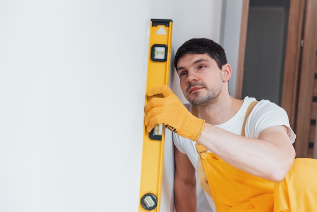 Handyman in yellow uniform checks levels of wall House renovation conception