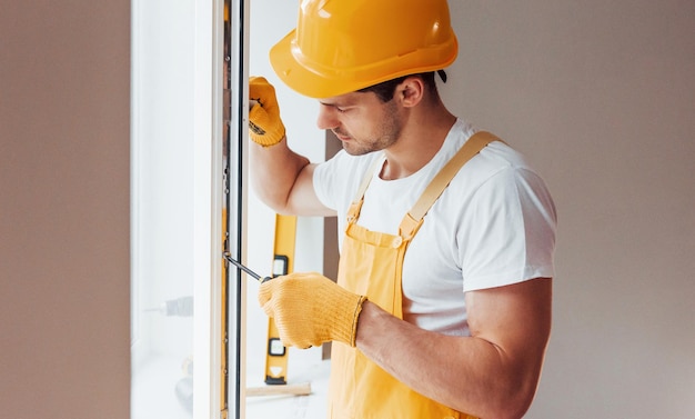 Handyman in yellow uniform installs new window House renovation conception