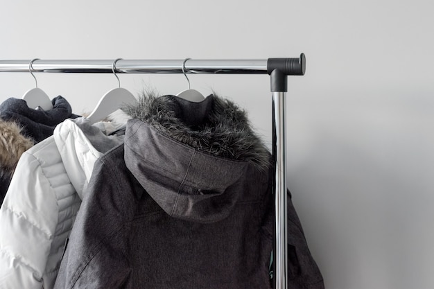 Hanger stand with warm jackets. Winter jackets with fur collar hang on white wooden hangers. 