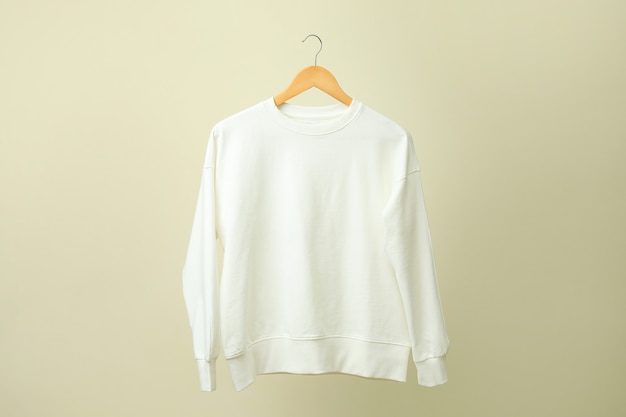 Hanger with white sweatshirt against beige surface