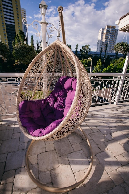 подвесной стул-кокон с фиолетовой подушкой на летней террасе ресторана