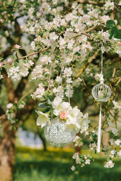Hanging decor in the form of a silver vase with flowers hanging on a flowering branch of an Apple tree in the spring in the garden