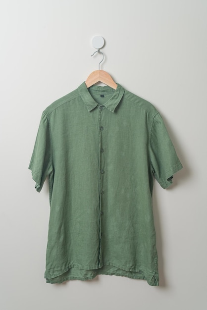 висит зеленая рубашка с деревянной вешалкой на стене