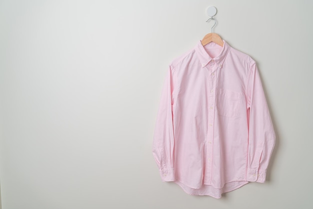 висит розовая рубашка с деревянной вешалкой на стене