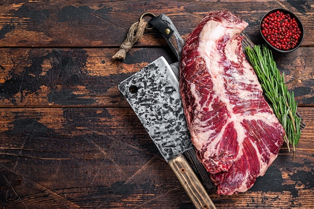 Hanging tender or hanger raw beef meat steak on butcher board with cleaver. Dark wooden background. Top View. Copy space.