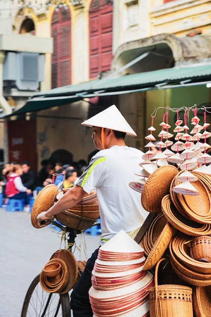 Hanoi, Vietnam - 21 februari 2016: Man op de fiets die traditionele Vietnamese hoeden verkoopt op de straatmarkt in Hanoi, Vietnam