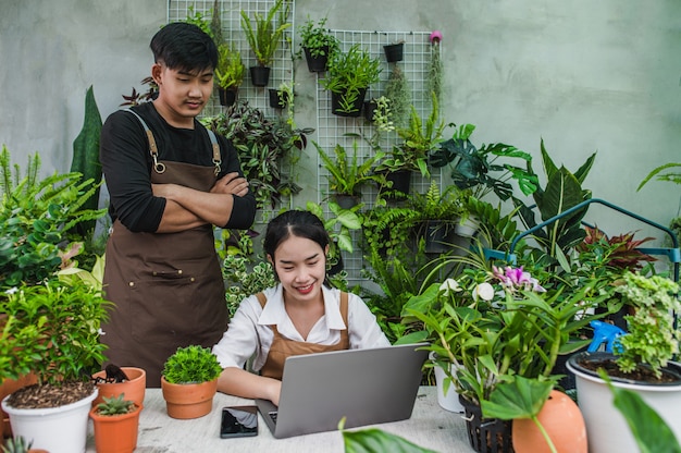 Happily gardener couple use laptop computer while online tutorial on potted plans in workshop together