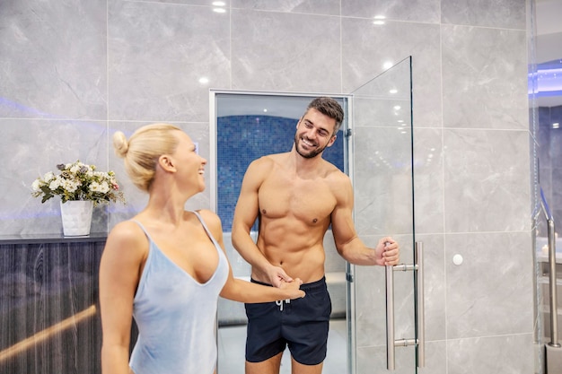 A happily married couple in swimwear holding hands and entering the room in spa and wellness center