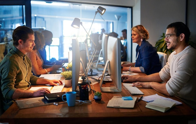 Photo happily working those long hours shot of a team of young businesspeople working late in the office