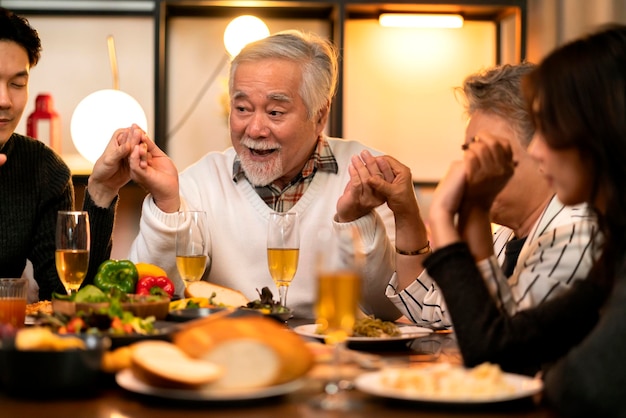 Felicità asiatica multigenerazione che pranza insiemefamiglia tenendosi per mano e pregando per il ringraziamento prima della cena delle vacanzenonno nipoti stare insieme nella cena tradizionale del ringraziamento a casa