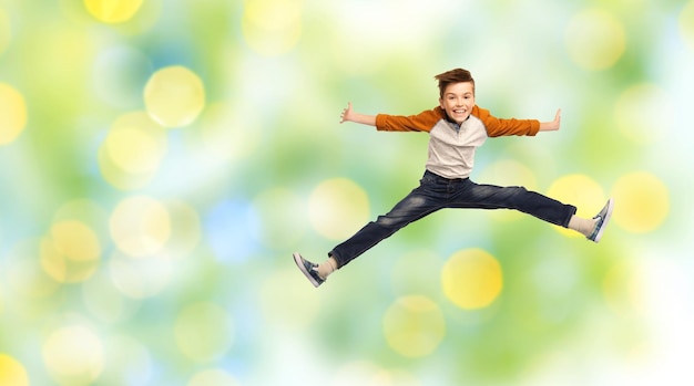 happiness, childhood, freedom, movement and people concept - happy smiling boy jumping in air over green summer holidays lights background