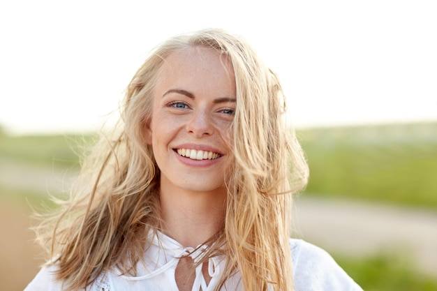 happiness, country, summer holidays, vacation and people concept - close up of happy smiling young woman or teenage girl with wild hair outdoors