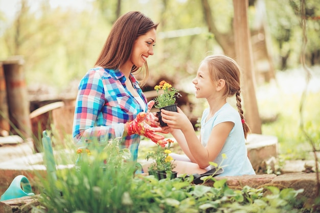 裏庭に花を植える彼女の笑顔の母親を支援する幸せかわいい女の子。