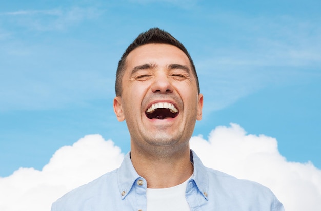 happiness, emotions and people concept - laughing man over blue sky and cloud background